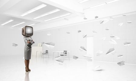 Business woman in suit with an old TV instead of head keeping arms crossed while standing among flying paper planes inside office building. 3D rendering.の写真素材
