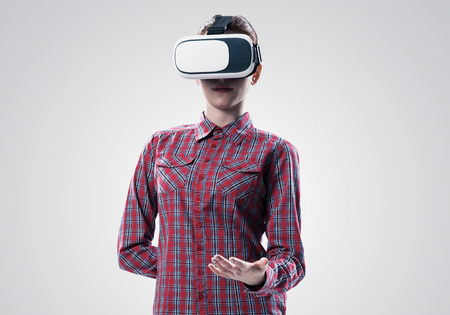 Young woman in checked shirt wearing virtual helmet against gray backgroundの写真素材