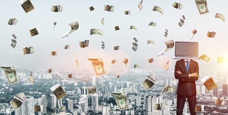 Cropped image of businessman in suit with laptop instead of head keeping arms crossed while standing outdoors among flying dollars planes with cityscape view on background.の写真素材