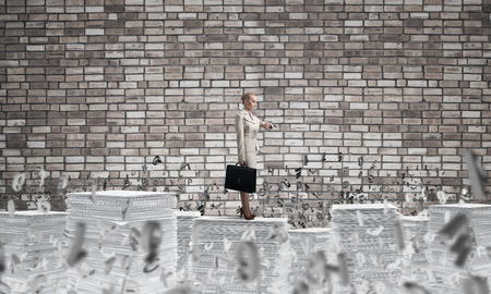 Confident business woman in suit standing among flying letters with brick wall on background. Mixed media.の写真素材
