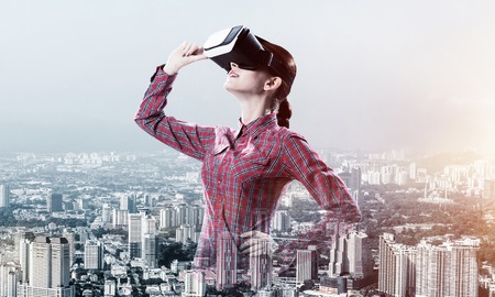 Young caucasian woman in virtual reality helmet against cityscape backgroundの写真素材