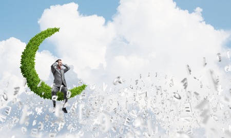 Frustrated businessman sitting on green moon and closing ears with handsの写真素材