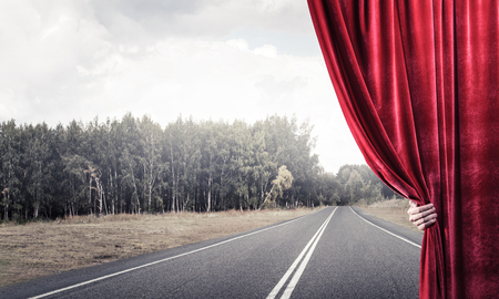 Human hand opens red velvet curtain to landscape with roadの写真素材