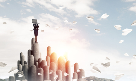 Business woman in suit with laptop instead of head keeping arms crossed while standing on the top of stone column with beautiful skyscape on background. 3D rendering.の写真素材