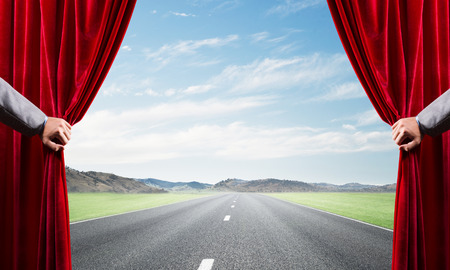 Human hand opens red velvet curtain to landscape with roadの写真素材