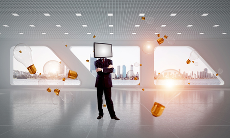 Businessman in suit with TV instead of head keeping arms crossed while standing among flying and glowing lightbulbs inside office building. 3D rendering.の写真素材
