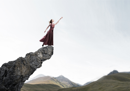 Young attractive woman relaxing in summer day standing on rock topの写真素材
