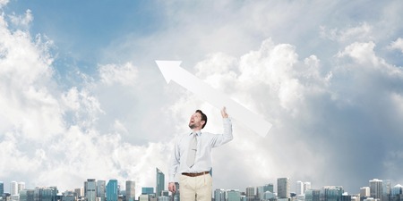 Horizontal shot of young businessman throwing big white arrow in the air while standing against...