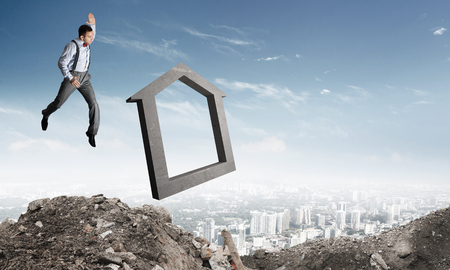Jumping businessman crashing big house symbol with city view on background. 3D rendering.の写真素材