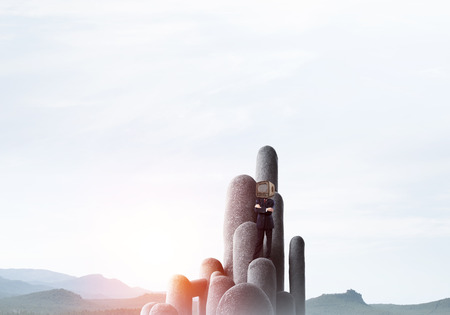 Businessman in suit with an old TV instead of head keeping arms crossed while standing on the top of stone columns with beautiful landscape on background.の写真素材