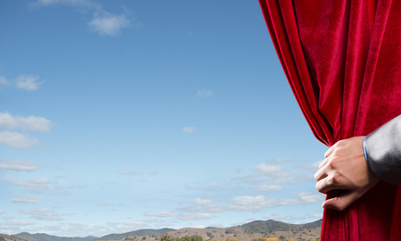 Human hand opens red curtain on natural landscape backgroundの写真素材