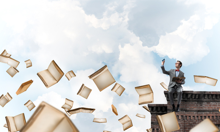 Funny man in red glasses and suit sitting on building top and reading bookの写真素材