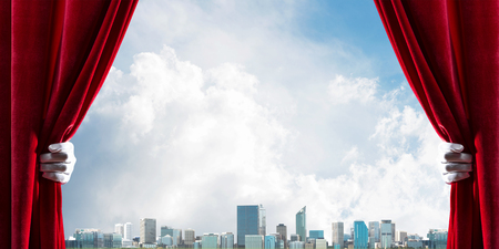 Human hand in glove opens red velvet curtain to modern cityscapeの写真素材