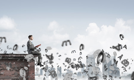 Young businessman sitting on building top with red book in handsの写真素材