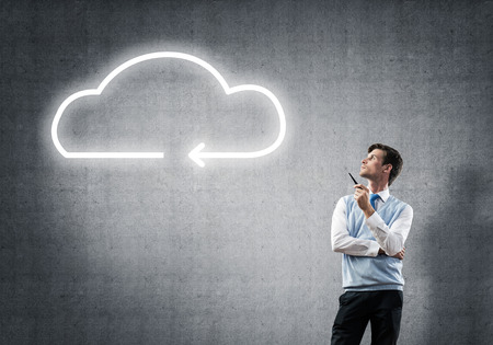 Confident and young businessman smoking pipe and drawn cloud on gray wall backgroundの写真素材