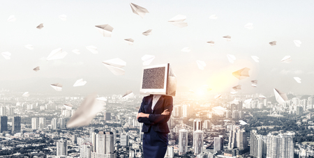 Cropped image of business woman in suit with monitor instead of head keeping arms crossed while standing outdoors among flying paper planes with cityscape view on background.の写真素材