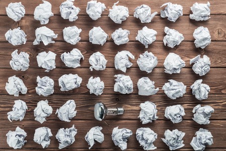 Incandescent bulb and crumpled white paper balls on brown wooden tableの写真素材