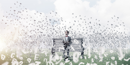 Funny man in red glasses and suit sitting on bench and reading bookの写真素材