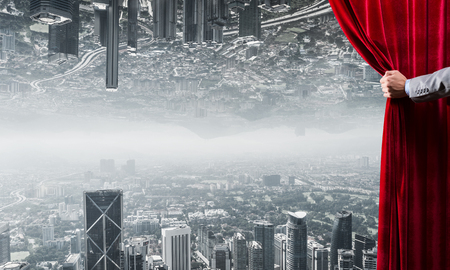 Hand of businessman opening red velvet curtain and cityscape at backgroundの写真素材