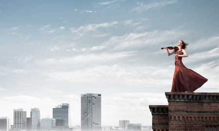 Young attractive girl playing violin at top of building. Mixed mediaの写真素材