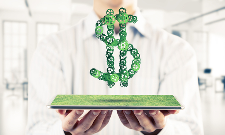 Close of businessman holding tablet pc with dollar sign made of gears. Mixed mediaの写真素材