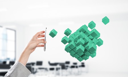 Close of businesswoman hand holding smartphone and cube figure out of screen. Mixed media