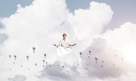 Man in white clothing keeping eyes closed and looking concentrated while meditating among flying aerostats in the air with cloudy skyscape on background.の写真素材
