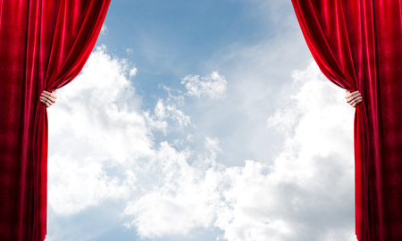 Human hand opens red velvet curtain on blue sky backgroundの写真素材