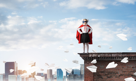 Young girl in superhero costume standing on building roof. Mixed mediaの写真素材