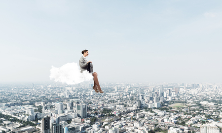 Young elegant woman with suitcase in hands siting on cloudの写真素材