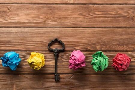 Vintage key among many balls of crumpled paper on wooden table