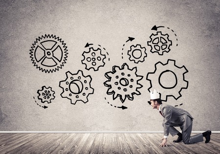 Young handsome businessman wearing white paper crown running and gear mechanism on wallの写真素材