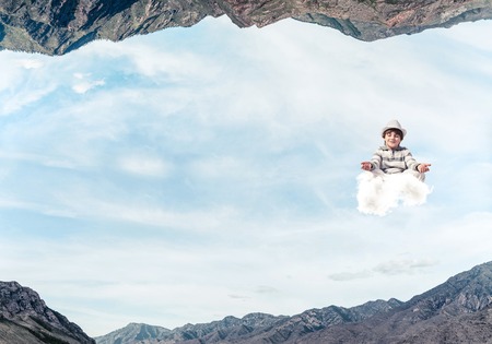 Young boy keeping eyes closed and looking concentrated while meditating on cloud in the air between two nature worlds.の写真素材