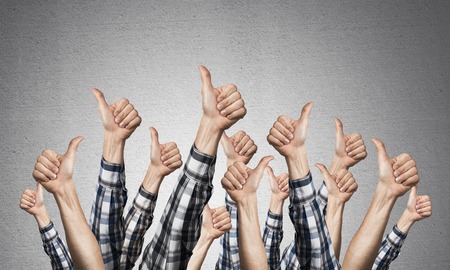 Row of man hands showing thumb up gesture. Agreement and approval group of signs. Human hands gesturing on background of grey wall. Many arms raised together and present popular gesture.の写真素材
