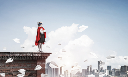 Young girl in superhero costume standing on building roof. Mixed mediaの写真素材