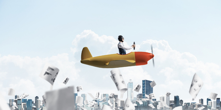 Business accounting and statistics concept with funny pilot. Aviator driving propeller plane above falling paper sheets with infographics. Young man flying in small airplane above paperwork.の写真素材
