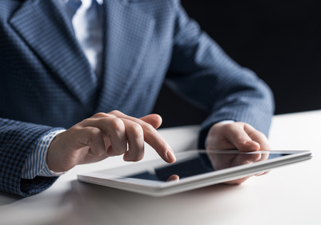 Close-up of male hand touching screen of digital tablet. Man in business suit sitting at desk and working at tablet computer. Manager at workplace in office. Business and digital technology conceptの写真素材