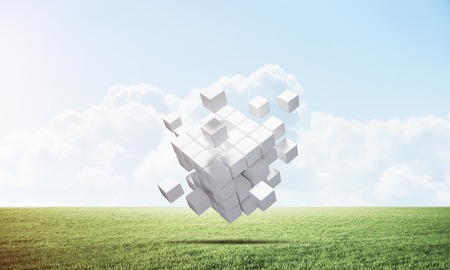 Abstract flying white cubes on green meadow. Virtual reality and digital technology. Hi-tech geometric composition. Nature landscape with green grass and blue sky. Mixed media with 3D rendering objectの写真素材