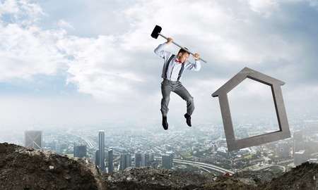 Jumping businessman crashing big house symbol with city view on background. 3D rendering.の写真素材