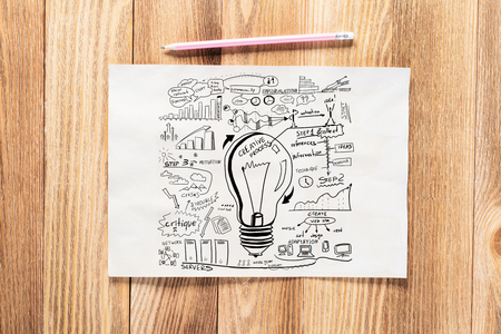 Business infographics pencil hand drawn with group of commercial doodles. Top view of workplace with paper and pencil lying on wooden desk. Financial statistics and analytics. Light bulb and chartsの写真素材