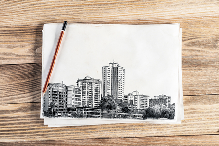 Modern city center pencil draw. Urban architecture hand drawn sketch on wooden table. Sheet of paper on textured natural wooden background. Architecture agency template. View from above with copyspaceの写真素材