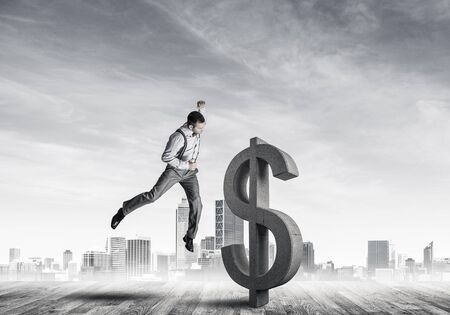 Young furious businessman going to crash with fist stone dollar symbolの写真素材