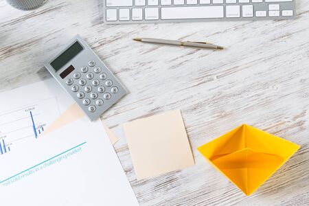 Businessman workspace with office desk and yellow paper ship. Marketing and advertising. Flat lay wooden table with computer keyboard, calculator and pen. Creative project management concept.の写真素材