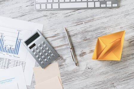 Businessman workspace with office desk and yellow paper ship. Marketing and advertising. Flat lay wooden table with computer keyboard, calculator and pen. Creative project management concept.の写真素材