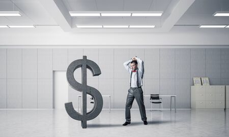 Young furious businessman going to crash with hands stone dollar symbolの写真素材