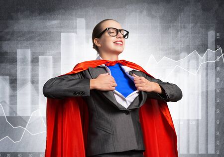 Portrait of business woman super heroine tearing off her shirt. Smiling business lady with closed eyes in red hero cape on financial diagram background. Brave super woman dreaming about new winsの写真素材
