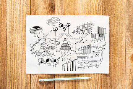 Investment statistics and analytics pencil hand drawn with group of business doodles. Financial charts and graphs. Strategy planning and analysis. Workplace with paper and pencil lying on wooden desk.の写真素材