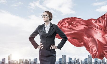 Young confident businesswoman wearing red cape against modern city backgroundの写真素材