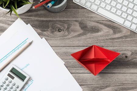 Businessman workspace at office desk with red paper ship. Top view office workplace background. Flat lay table with computer keyboard, calculator, business reports and pen. Main project managementの写真素材