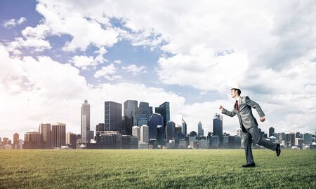 Young handsome businessman wearing white paper crown running in a hurryの写真素材